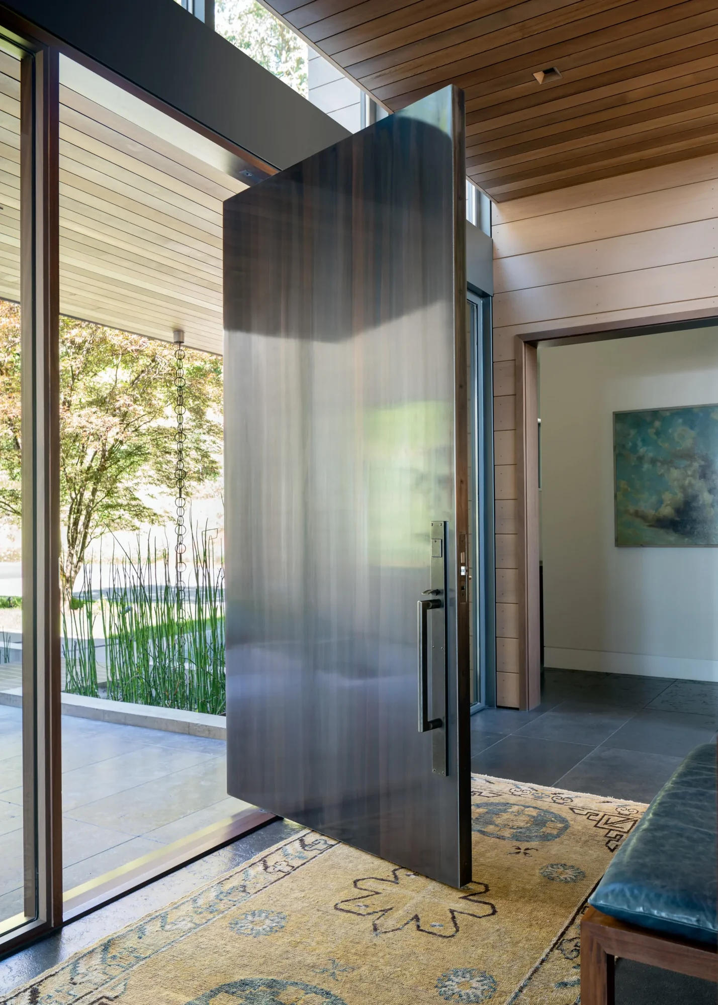 Modern entry with pivoting frosted glass door opening to courtyard with ornamental grasses and wood ceiling