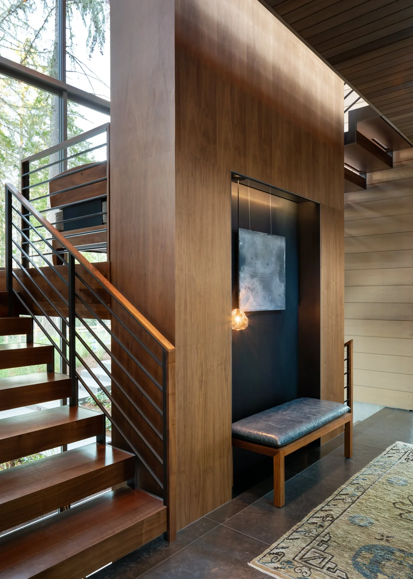 Modern entryway with wood-clad wall, floating staircase with metal railings, dark accent niche, and slate tile flooring.