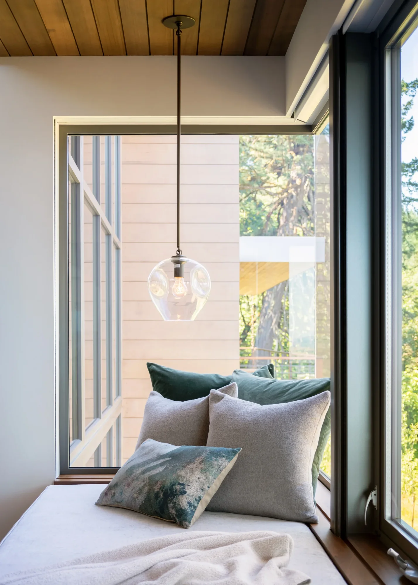 Cozy window seat with pillows and pendant light overlooking natural landscape through black-framed windows