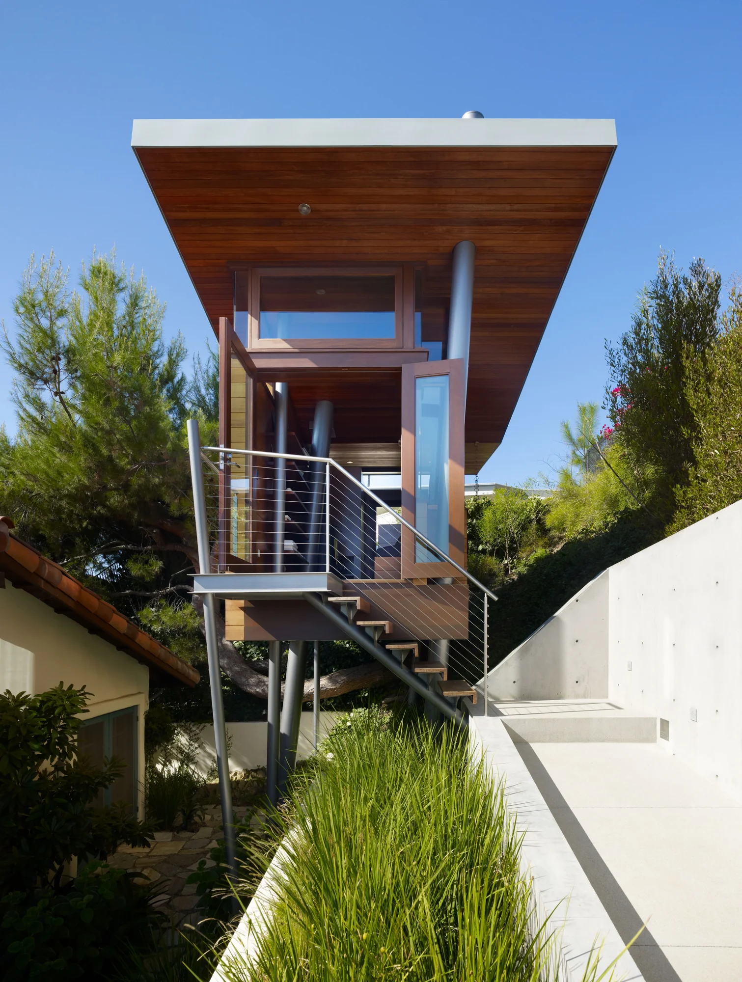 Modern tower structure with cedar cladding and steel supports surrounded by landscaping and concrete walls