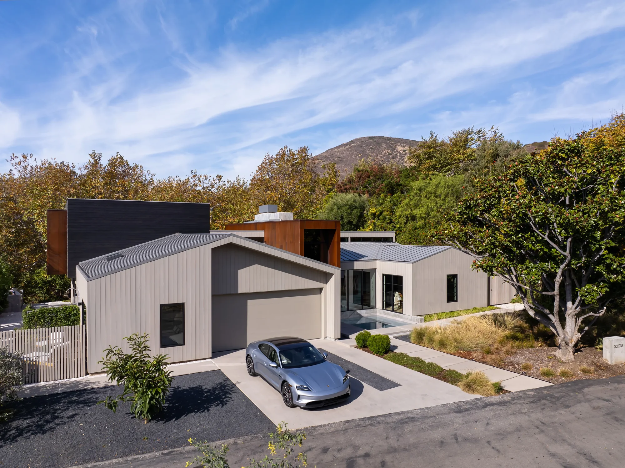 Modern single-story home with vertical siding and metal roof, featuring an attached garage and silver car in driveway with mountain backdrop.