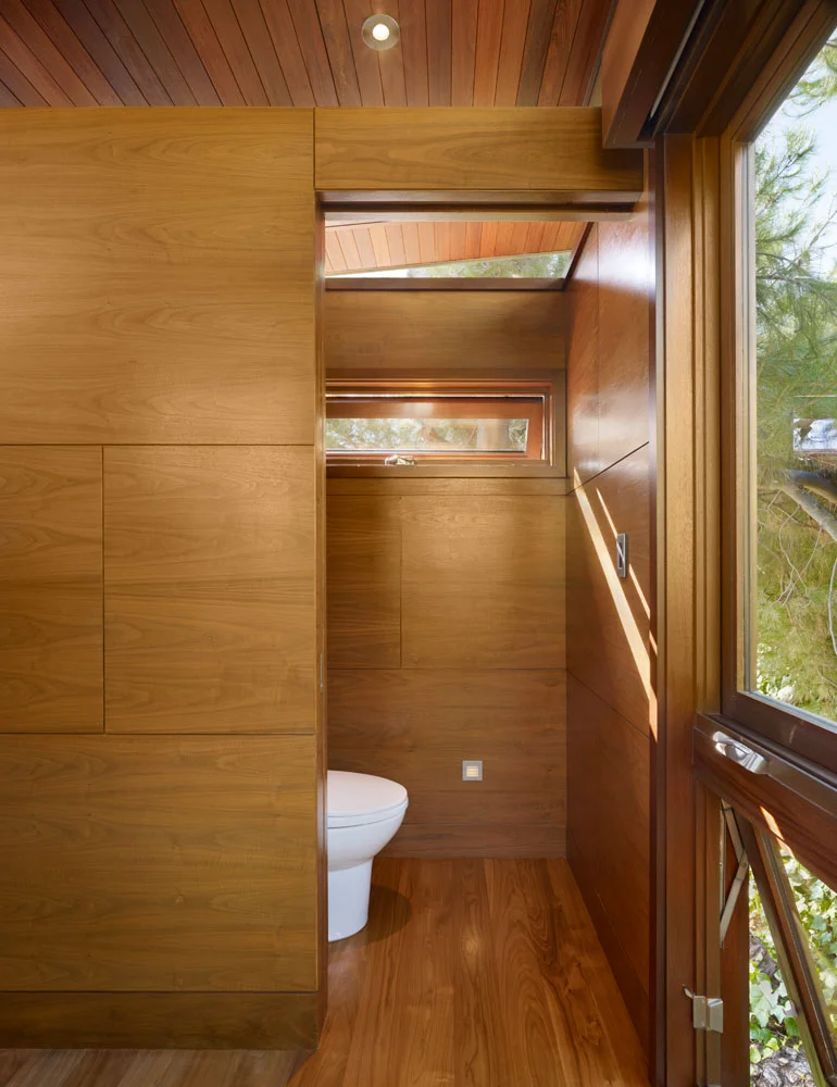 Compact bathroom with wood-paneled walls, horizontal window, and wood flooring in custom home