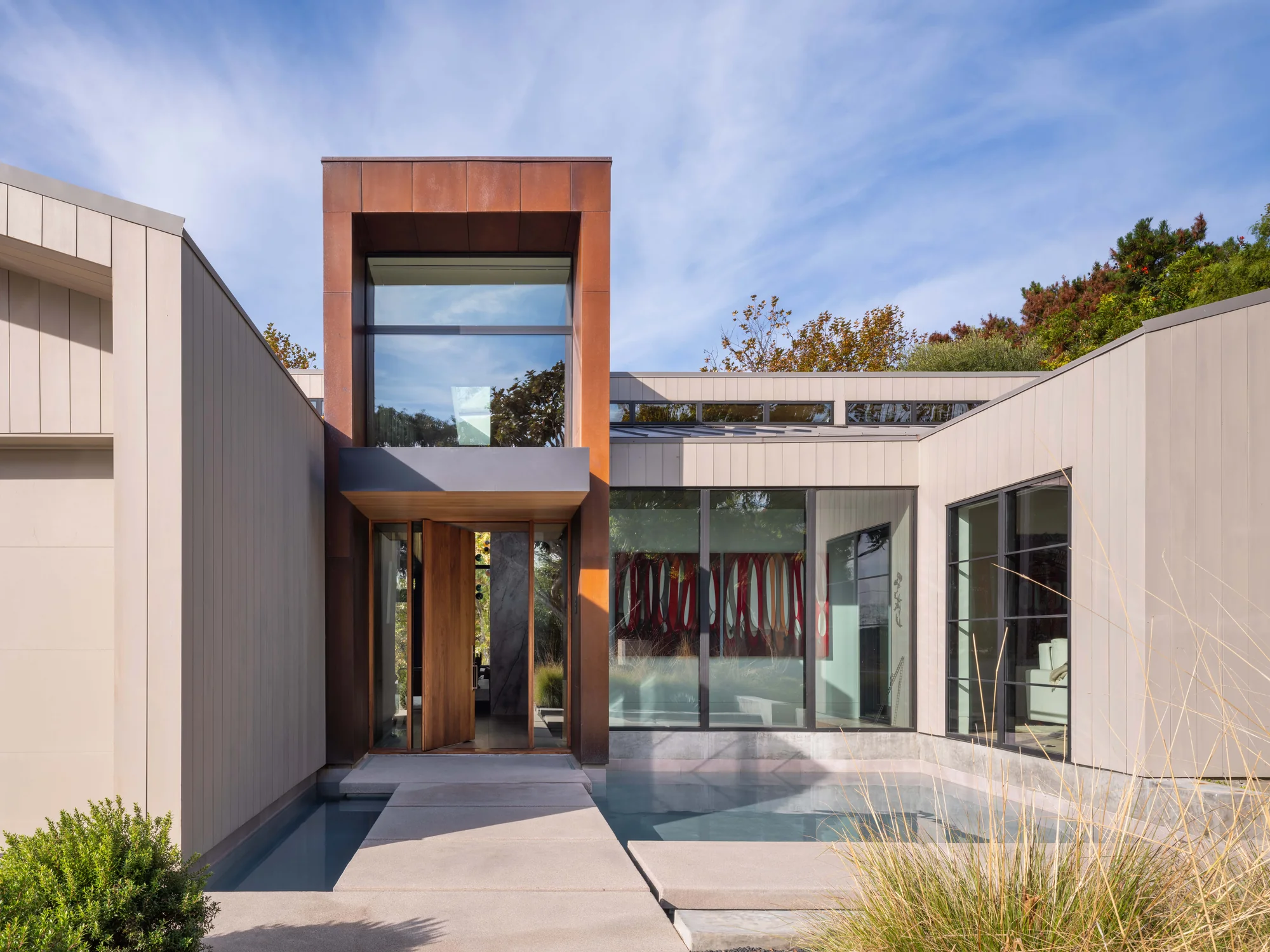 Modern home entrance with copper-clad tower, water feature, and courtyard blending indoor-outdoor living spaces.