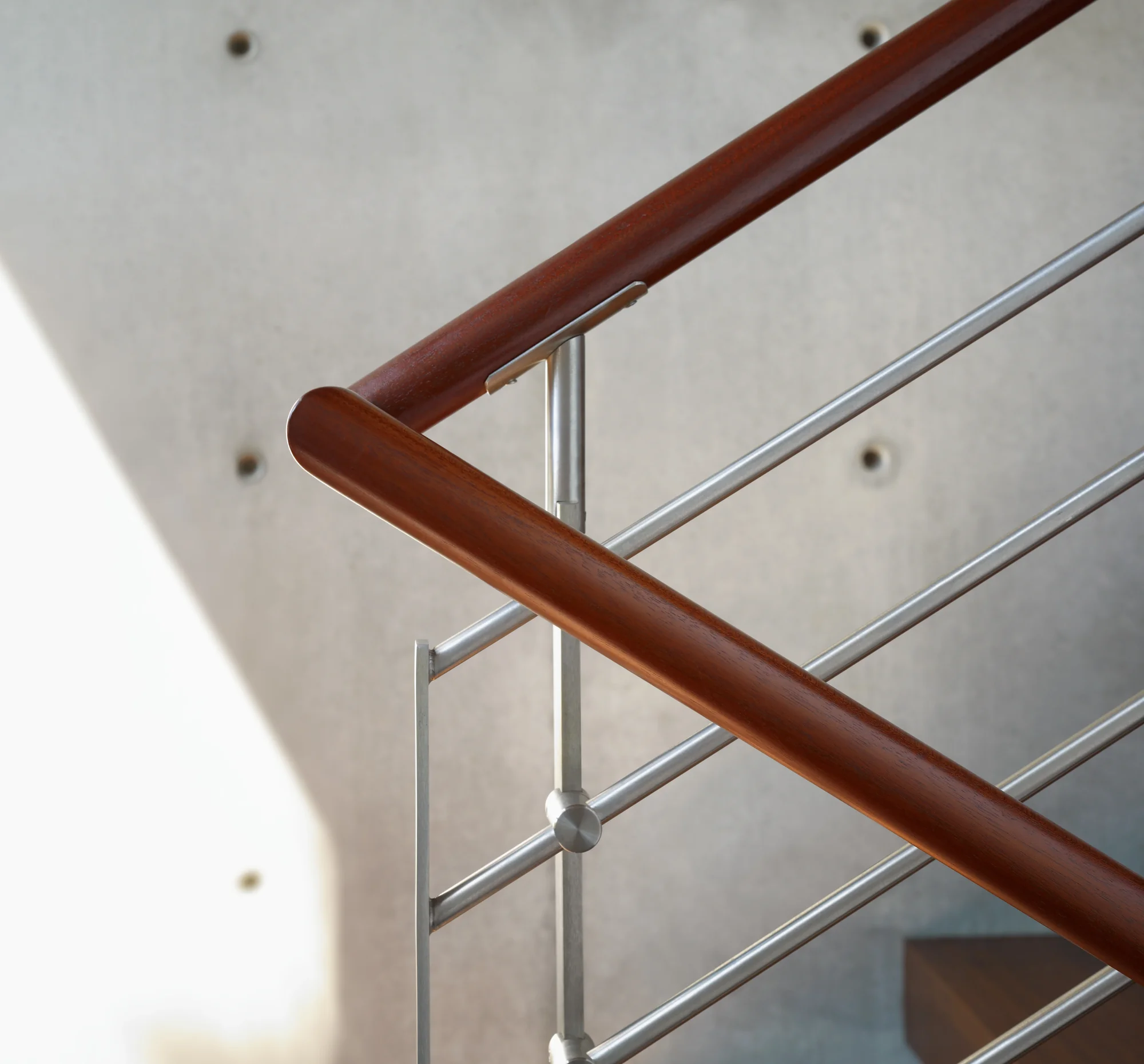 Close-up of a staircase railing featuring a smooth mahogany handrail supported by brushed stainless steel balusters.