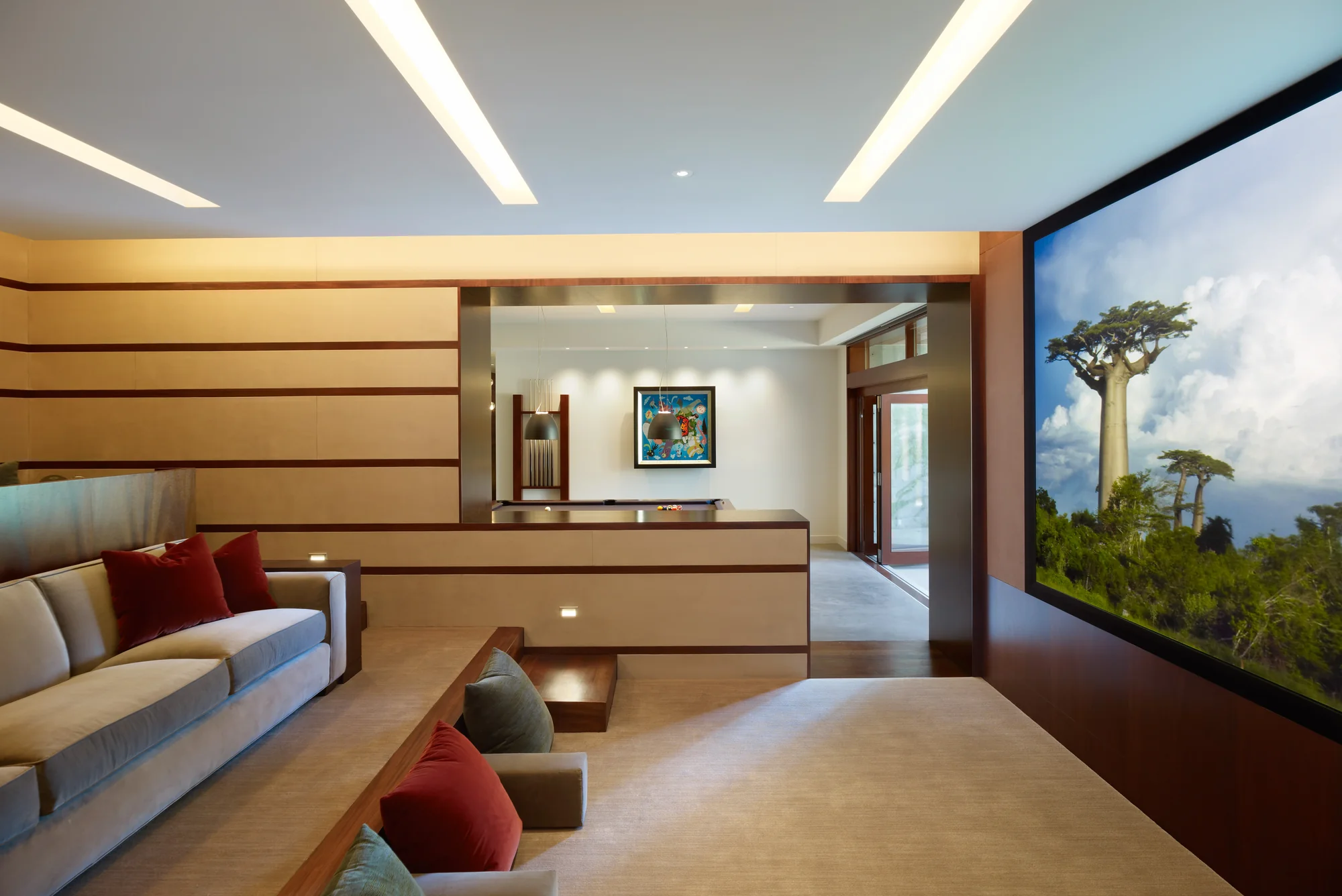 Luxury home theater with mahogany accents, recessed lighting, and a large nature mural depicting baobab trees against a blue sky.
