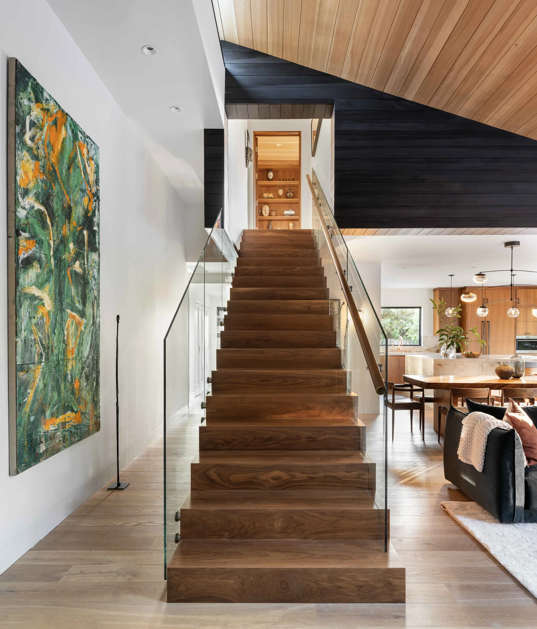 Modern wooden staircase with glass railing leading to upper floor, featuring warm walnut treads and cedar ceiling detail
