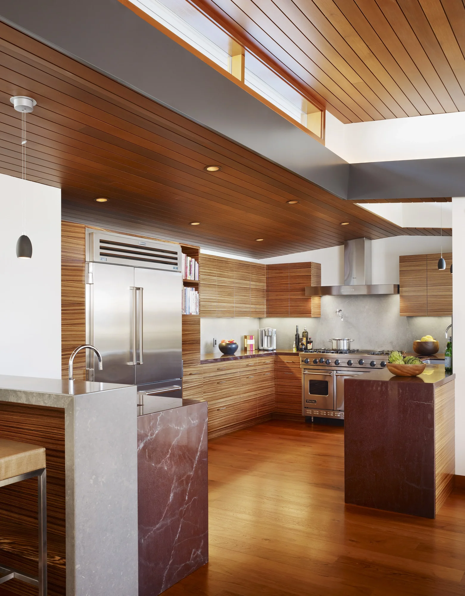 Modern kitchen with horizontal cedar cabinetry, wood-paneled ceiling, marble island, and stainless steel appliances