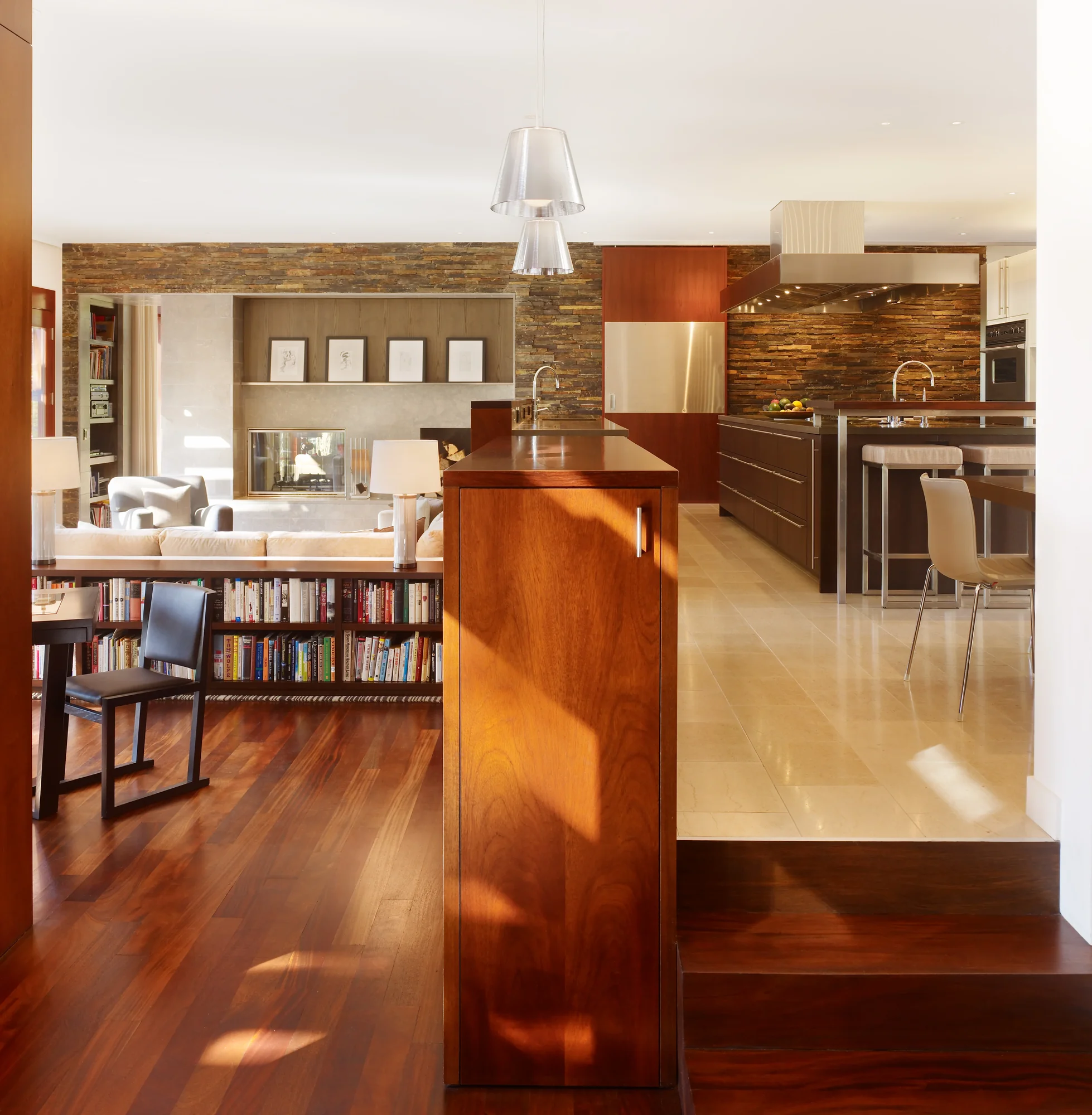 Open-plan interior with rich mahogany floors, stone accent walls, built-in bookshelves, and seamless kitchen-living flow.