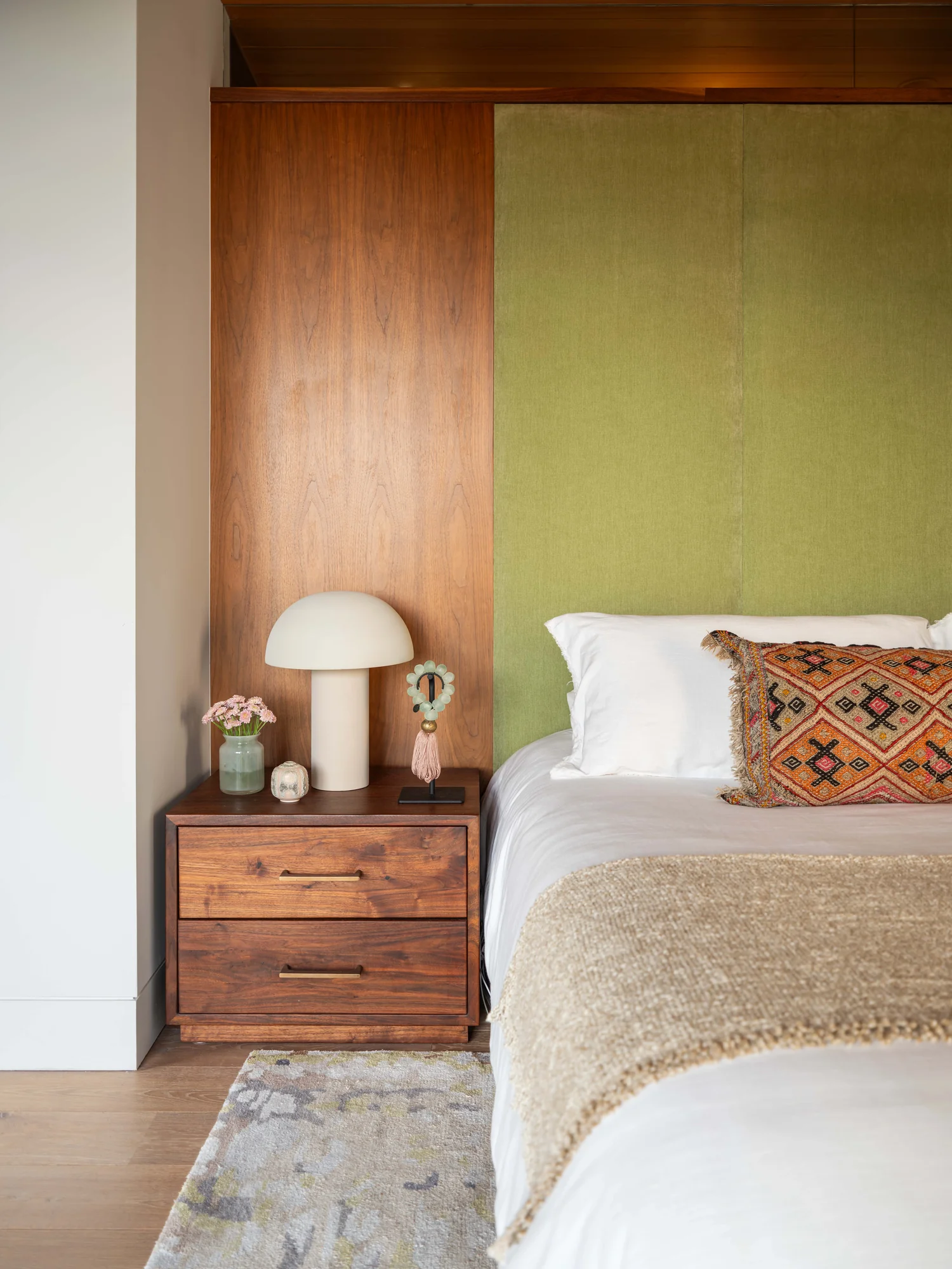 Modern bedroom with lime green upholstered headboard, walnut nightstand, and mushroom lamp against wood paneling.