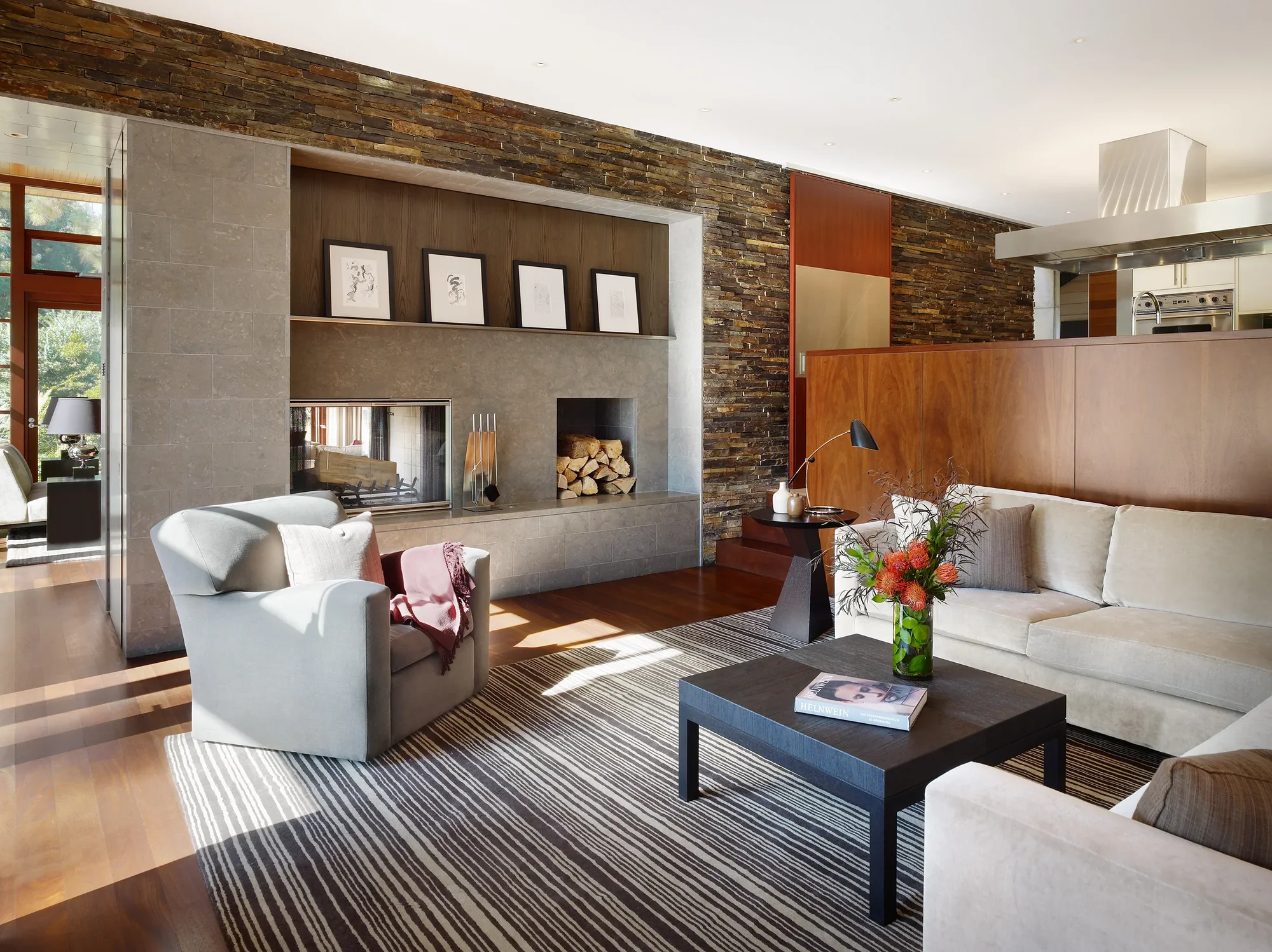 Modern living room with stone fireplace wall, wood accents, and striped rug connecting indoor and outdoor spaces.