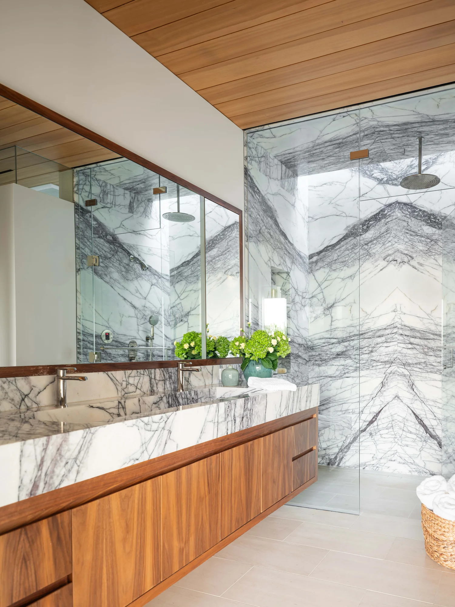 Luxurious bathroom with book-matched marble walls, walnut vanity, and glass-enclosed shower with wood ceiling.