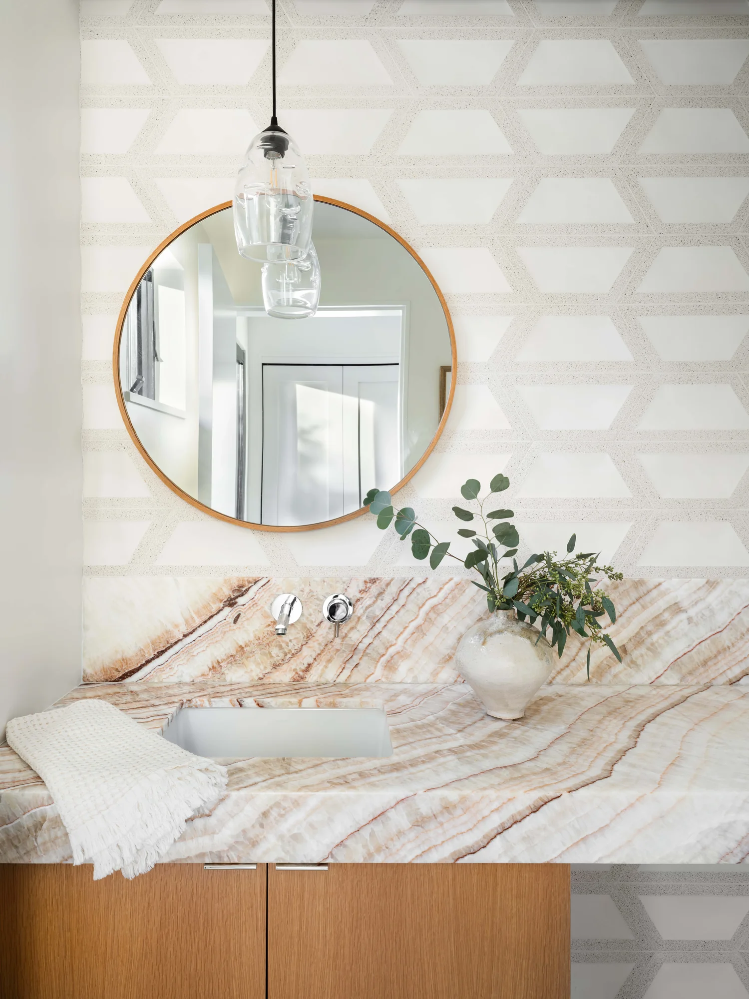 Modern bathroom vanity with striped marble countertop, round brass mirror, and geometric patterned wall tile