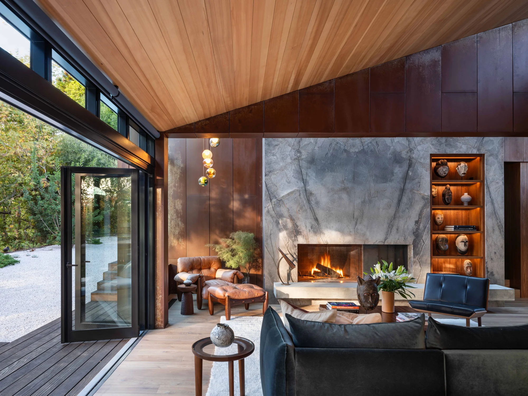 Modern living room with wood ceiling, marble fireplace, floor-to-ceiling windows opening to nature
