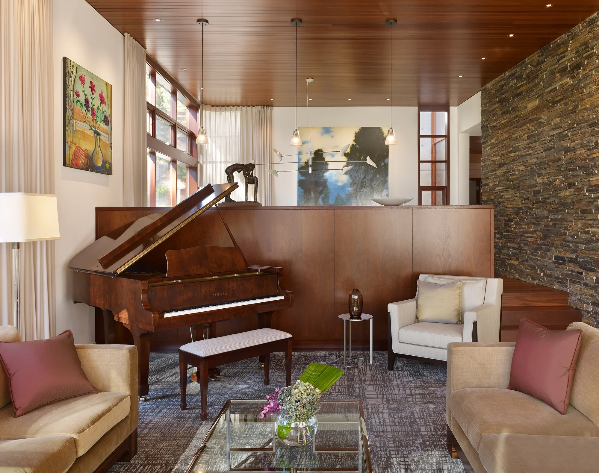 Elegant living room with mahogany grand piano, stacked stone accent wall, wood ceiling, and warm neutral furnishings.