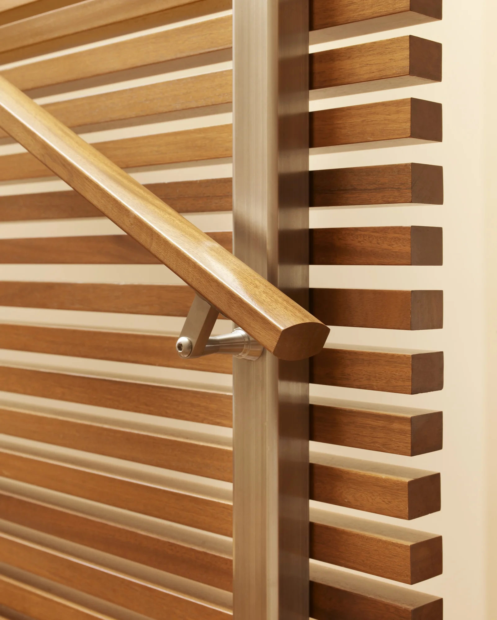 Modern wooden staircase detail showing mahogany handrail with metal brackets and horizontal slat railing system