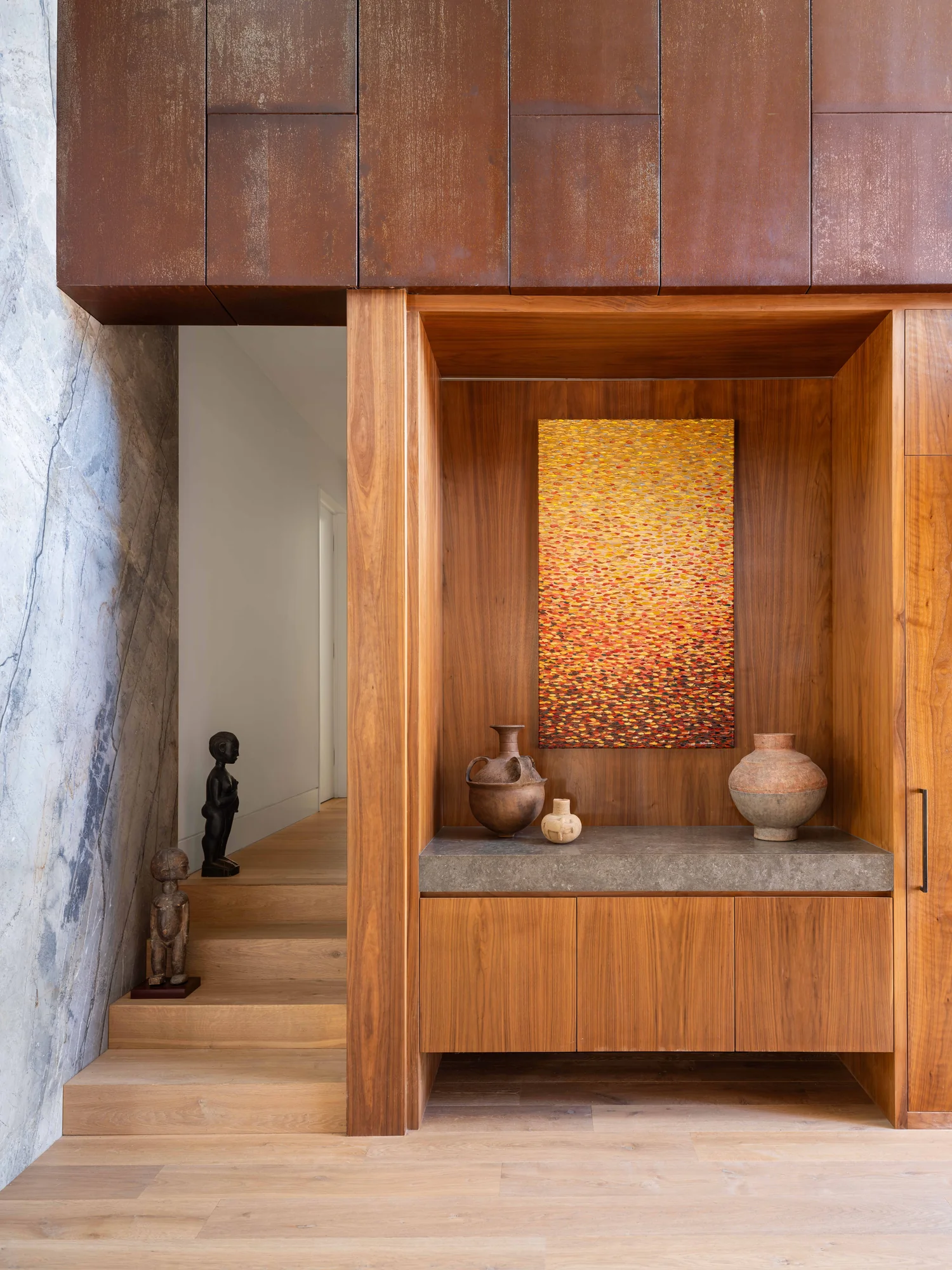 Custom wood display niche with concrete shelf, pottery, and artwork above stairway with weathered metal ceiling panels