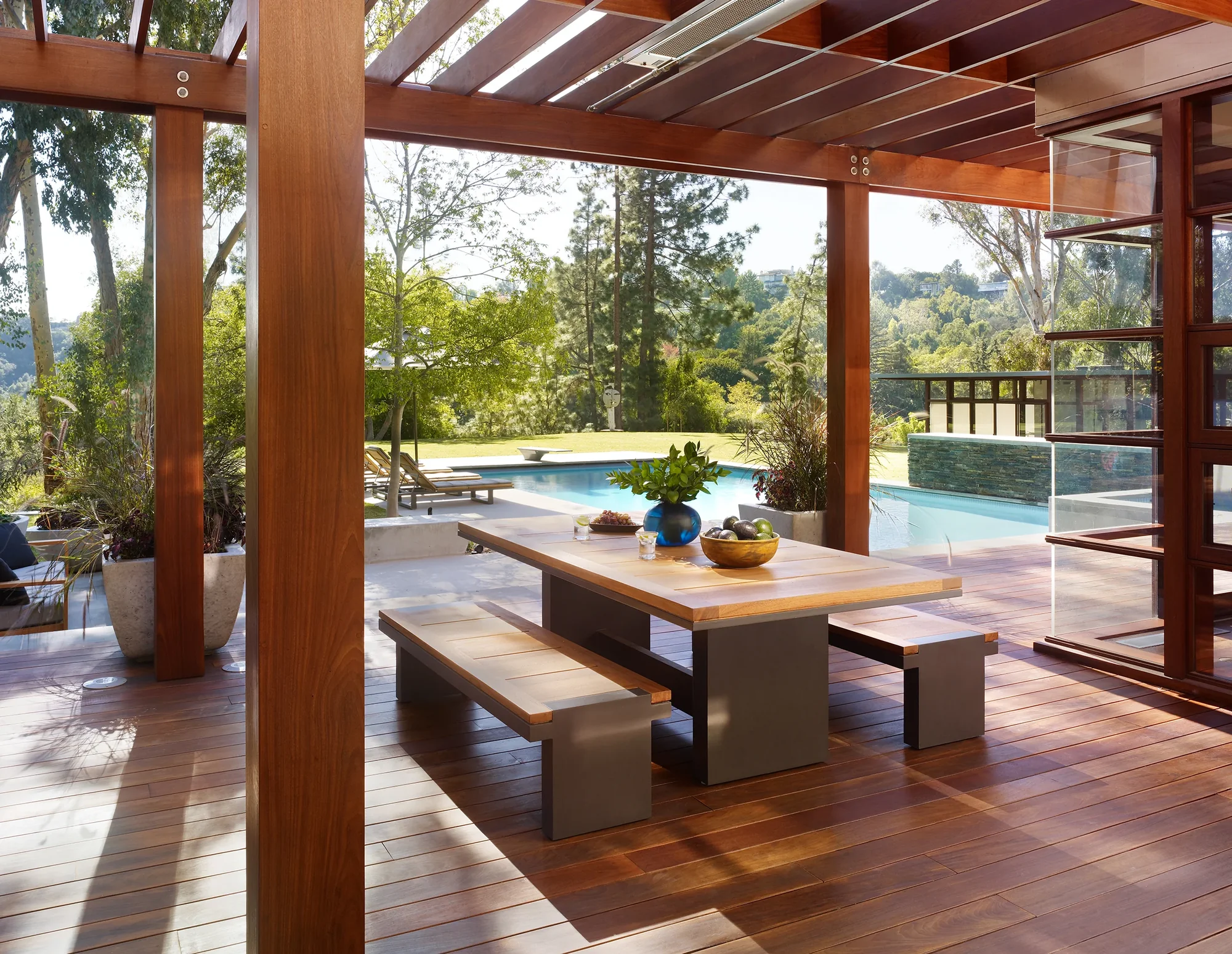 Covered outdoor dining area with mahogany table and benches overlooking pool and hillside landscape