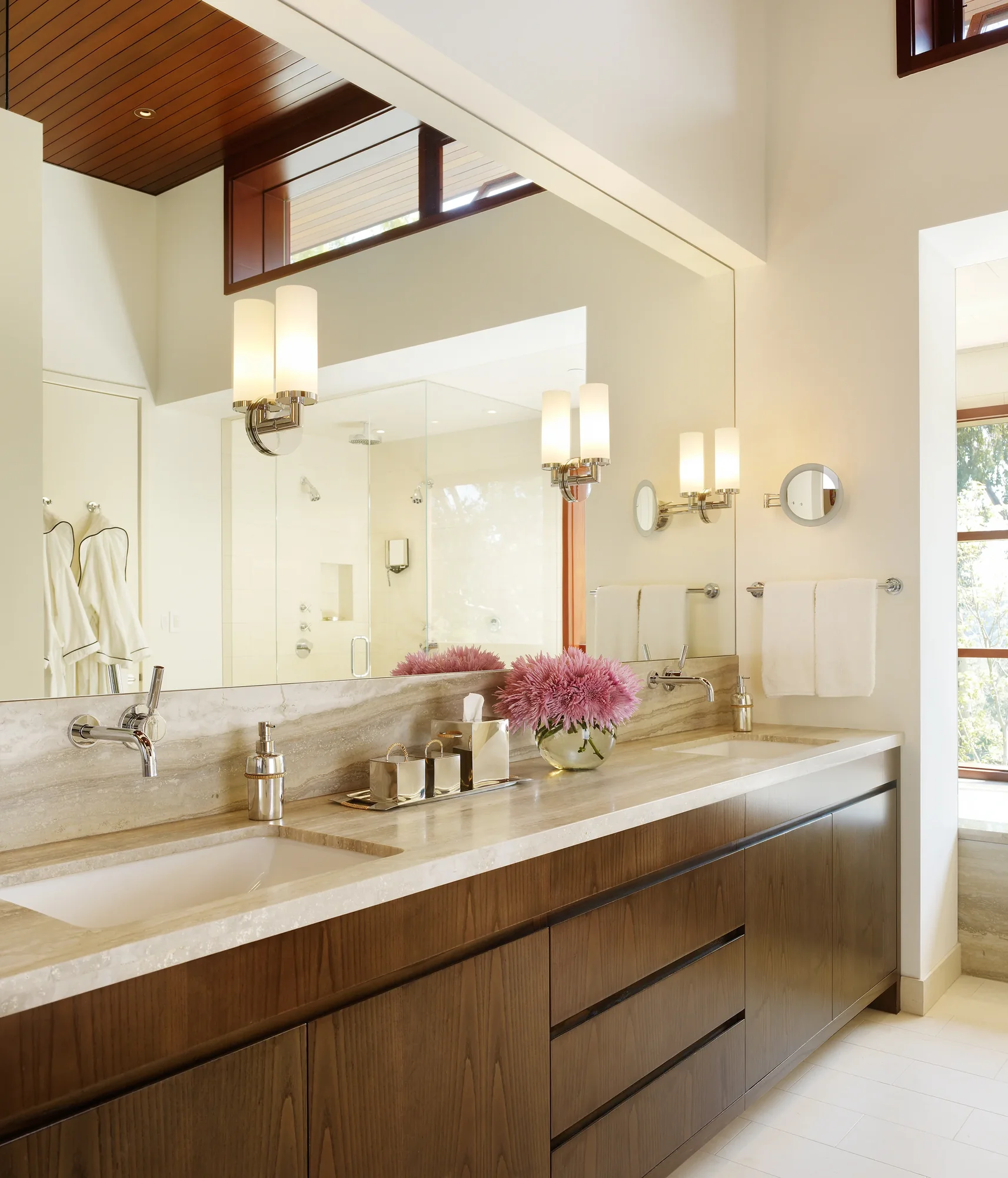 Luxury master bathroom with marble countertop, walnut vanity, wall-mount fixtures, and large mirror reflecting natural light.
